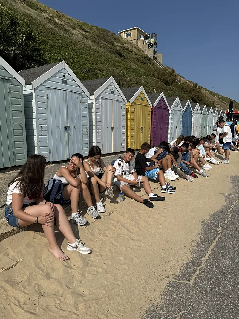 Students sat in front of beach huts on a school excursion